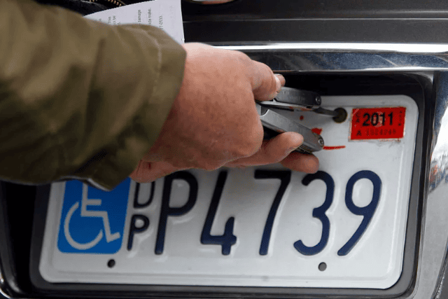 A male removing a disabled person plate from car.