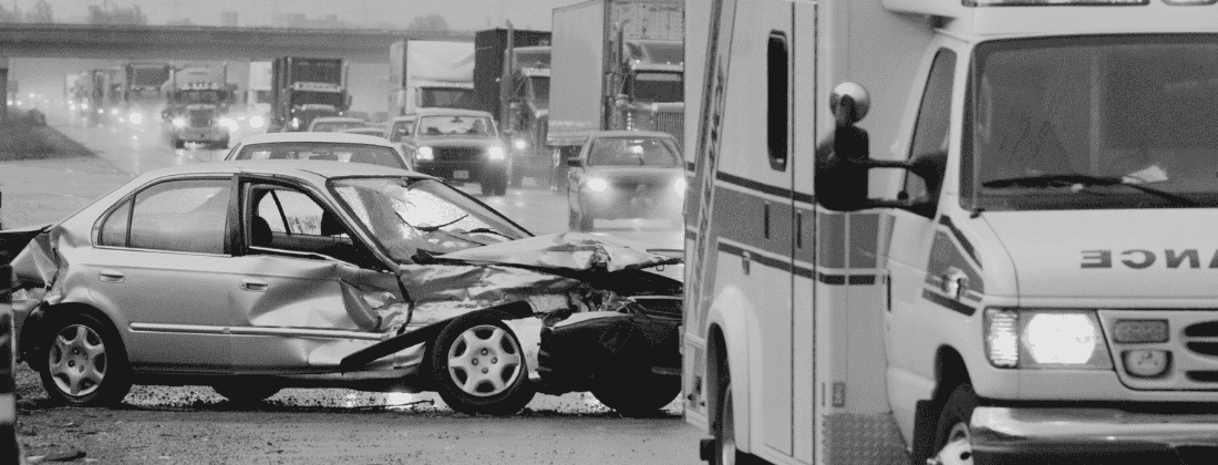 Scene of a car crash showing an ambulance responding and damaged vehicles on the roadway.