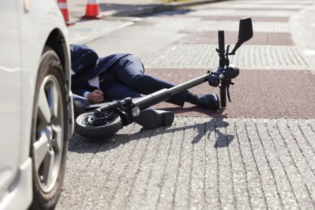 Electric scooter accident showing man on the ground in front of a car