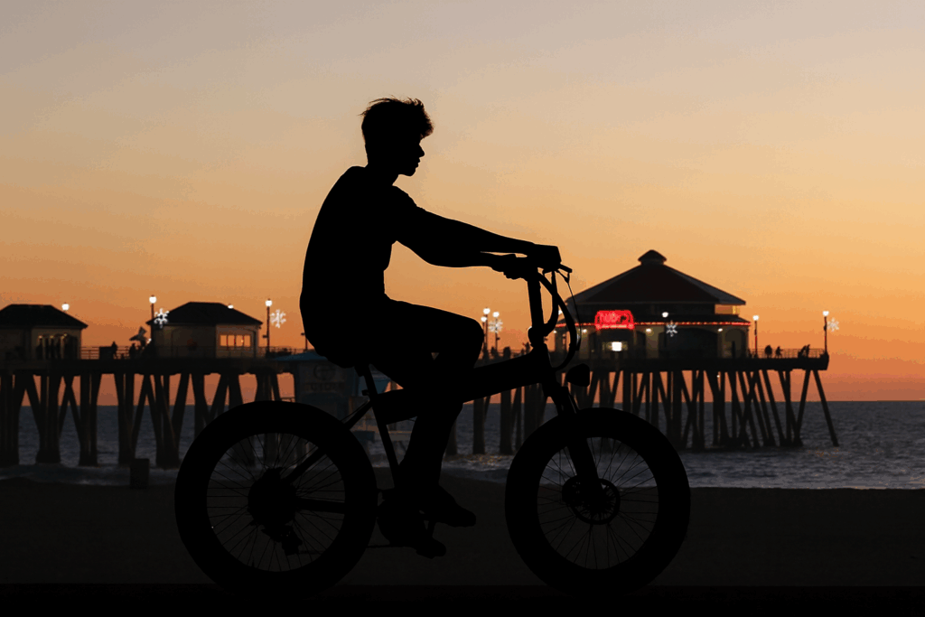Image of a teenager riding an electric bicycle at sunset; Huntington Beach pier is visible in the distance.