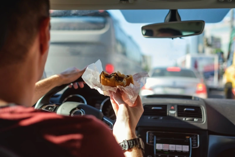 person eating a burger while driving in traffic